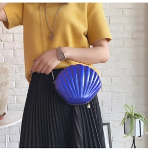 Detail of purple shell-shaped crossbody bag with pearl pendant and gold chain on model