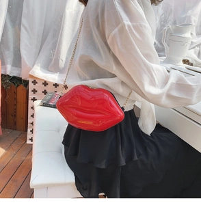 Detail of a bright red lip-shaped crossbody bag with a gold chain strap and glossy finish
