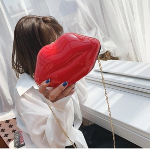 Detail of red lip-shaped crossbody bag with gold chain strap worn by a model