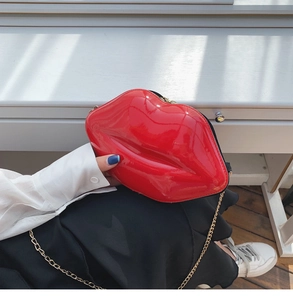 Detail of red lip-shaped glossy patent leather crossbody bag with gold chain strap