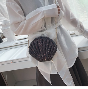 Detail of shell-shaped crossbody bag with glitter finish, gold chain, and pearl zipper