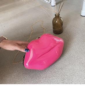 Close-up of a pink lip-shaped crossbody bag with glossy finish and gold chain strap