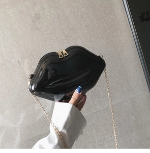 Detail of black glossy lip-shaped crossbody bag with gold chain strap and zipper