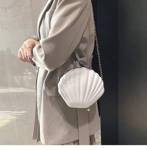 Chic white shell-shaped acrylic crossbody bag with gold chain strap worn by a model