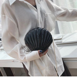 Detail of black shell-shaped acrylic crossbody bag with glossy finish and gold chain