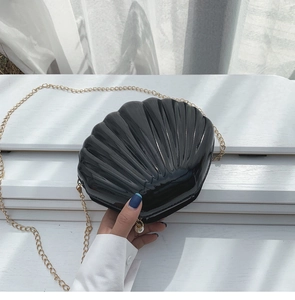 Detail of a black shell-shaped crossbody bag with gold chain and pearl ornament