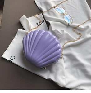 Macro shot of purple shell-shaped acrylic bag with gold chain and pearl clasp detail