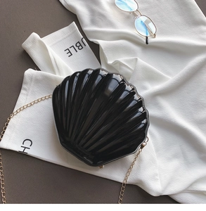 Detail shot of a black acrylic shell bag with pearl buckle and gold chain strap