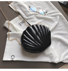 Close-up of black shell-shaped acrylic bag with gold chain and radiant texture details