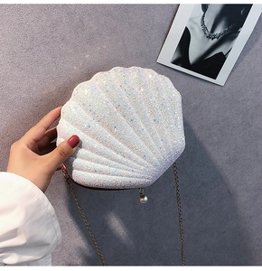 Detail of shell-shaped white sequined bag featuring a pearl charm and metal chain strap