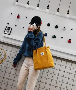 Detalle del bolso tote de pana amarilla con textura vertical y pequeña etiqueta blanca