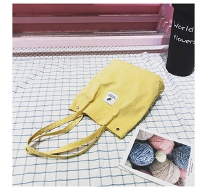 Détail du sac cabas en velours côtelé jaune montrant la texture et l'étiquette logo