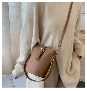 Detail of tan leather bucket bag with magnetic buckle closure and gold hardware