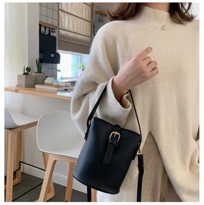 Detail of a chic black bucket bag with a gold buckle and adjustable strap on a model