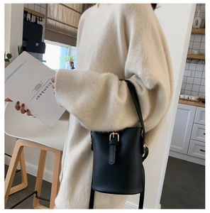 Detail of chic black bucket bag in matte leather worn with beige sweater