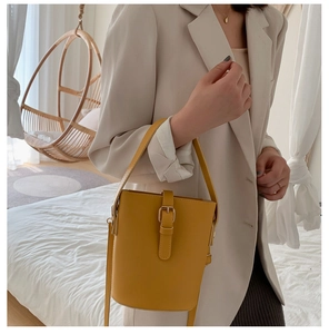 Detail of a ginger yellow bucket bag with decorative buckle and wide top handle