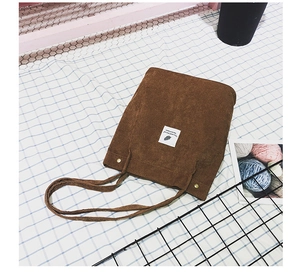 Détail du sac fourre-tout en velours côtelé marron avec étiquette plume et boutons dorés