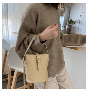 Detail of a chic beige mini bucket bag featuring a decorative metal buckle and PU leather texture