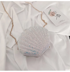 Detailed view of silver glitter shell cross-body bag with golden chain strap on fabric