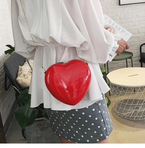 Nahaufnahme einer glänzenden roten Herztasche mit goldener Kette an einem Model
