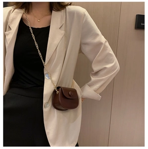 Detailopname van een bruine zadeltas met gouden ketting op een kaki kleurige blazer