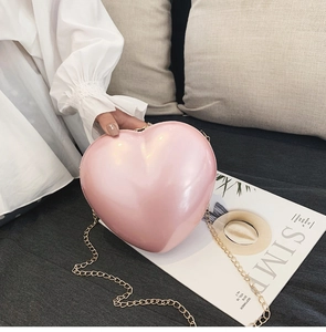 Rosafarbene herzförmige Umhängetasche mit Goldkette auf einem Sofa mit Magazinen