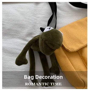 Close-up of green plush frog charm with X-shaped embroidery attached to a yellow canvas bag