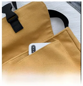 Detail showing the front pocket and black buckle of the yellow canvas messenger bag