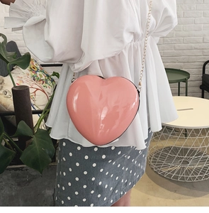 Detail der glänzenden pinken herzförmigen Mini-Umhängetasche mit goldener Kette am Model