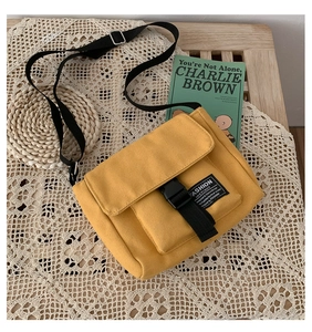 Detail of yellow canvas messenger bag featuring fashion patch and black buckle closure
