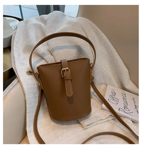 Detail of a brown leather bucket bag with metal buckle and adjustable shoulder strap