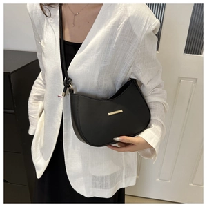 Minimalist black hobo shoulder bag with gold metal trim worn by model in white blazer