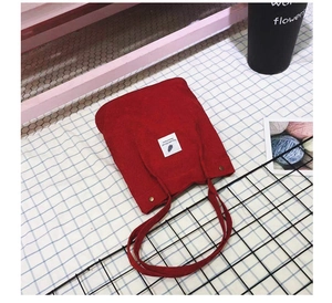 Détail du cabas en velours côtelé rouge foncé montrant la texture et le patch plume