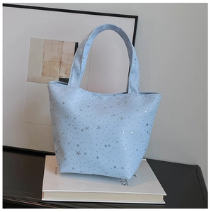 Close-up of light blue star sequin tote bag on book showing starry pattern and texture