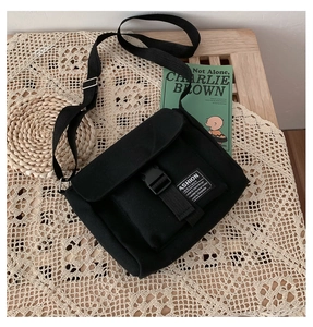 Detailed macro view of the black canvas messenger bag featuring a buckle strap and fashion label