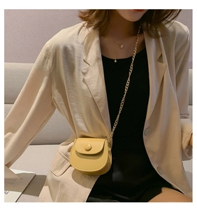 Detail van de lichtgele mini-zadeltas met gouden ketting gedragen over een beige blazer