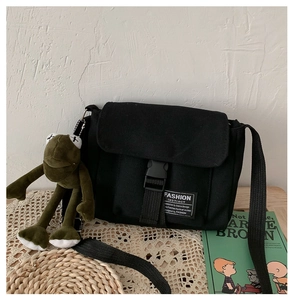 Detail of black canvas messenger bag featuring buckle closure and frog plush charm
