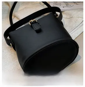 Detail of matte black bucket bag showing the oval base and gold buckle on a white texture
