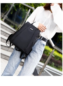 Detail showing high-density waterproof nylon fabric and sleek metal logo on black backpack