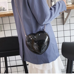 Moderne schwarze herzförmige Umhängetasche mit goldener Kette an einem Model präsentiert