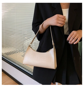 Close-up of off-white baguette bag with crocodile pattern and golden metal zipper