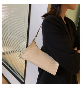 Detail view of cream crocodile-embossed baguette bag styled with a black blazer
