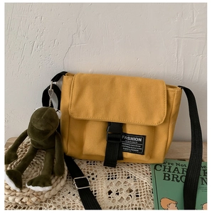 Detail of yellow canvas messenger bag featuring a buckle closure and green frog pendant