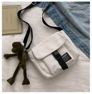 Detail of canvas messenger bag with adjustable buckle and green frog plush keychain