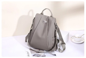 Detail of waterproof nylon backpack with elegant pleats and metal accent on gray surface