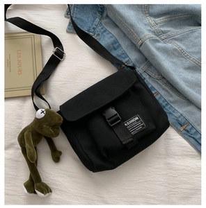 Detail of black canvas messenger bag with buckle closure and frog plush keychain charm
