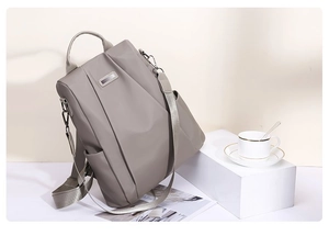Detail view of gray waterproof nylon backpack with metal logo and side pocket on a stand