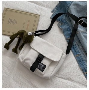 Detailed shot of white canvas crossbody bag with black buckle and cute frog plush pendant