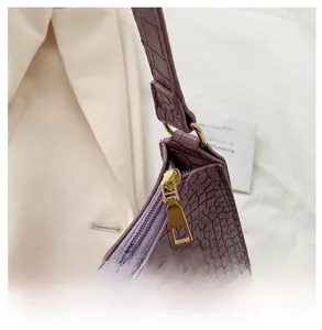 Detailed close-up of smooth gold zipper on purple crocodile texture baguette bag
