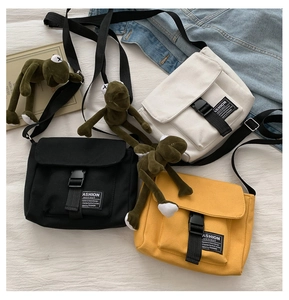 Detail of canvas messenger bags in black, beige and yellow with plush frog pendant